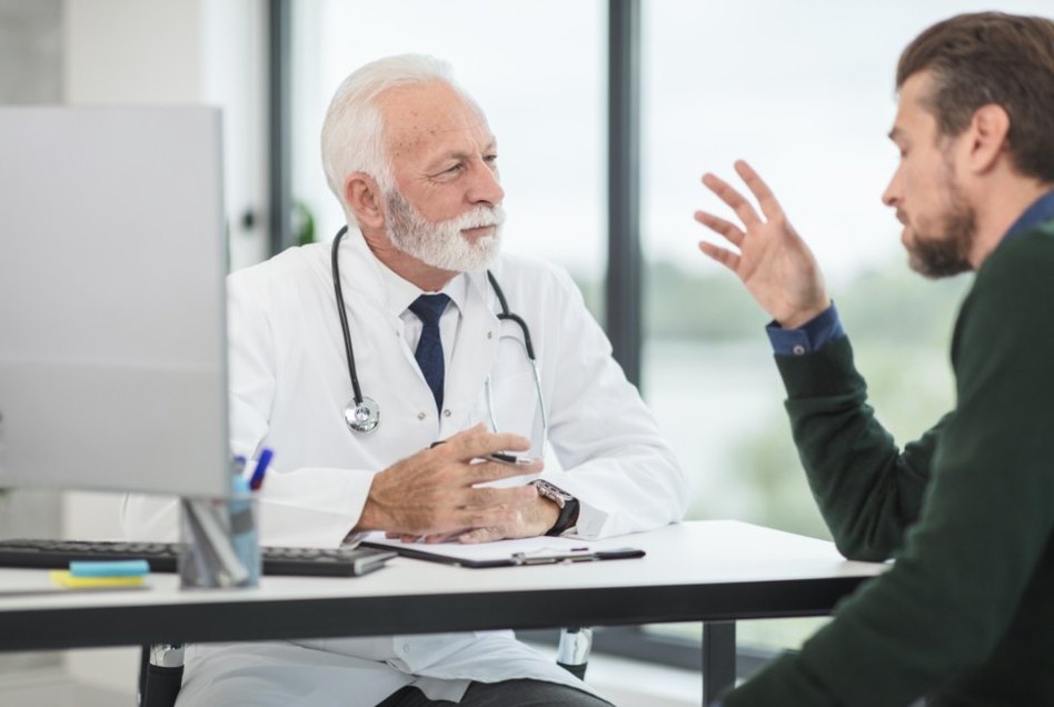 A clinician talking with a patient across the desk in a consulting room