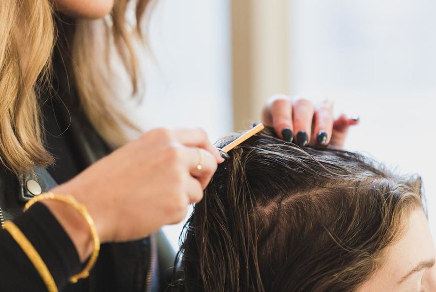 A hairdresser sectioning a client's hair with a comb at the salon chair